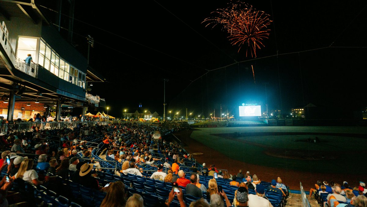 Fireworks over baseball field and crowd of people at nighttime