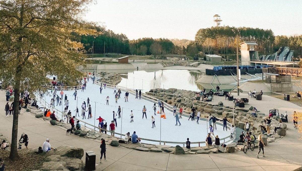 Far-away shot of people on ice skating rink with others walking on sidewalk surrounding it