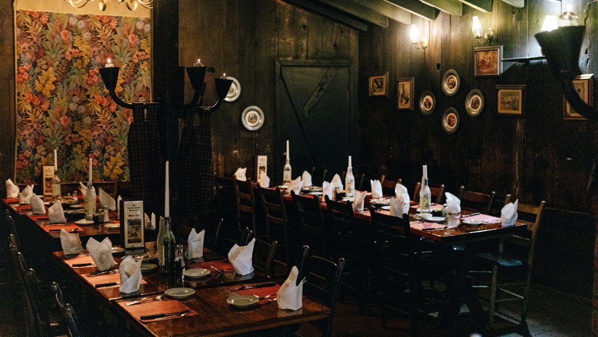 Interior of restaurant's dark dining with tables set and wall lamps lit