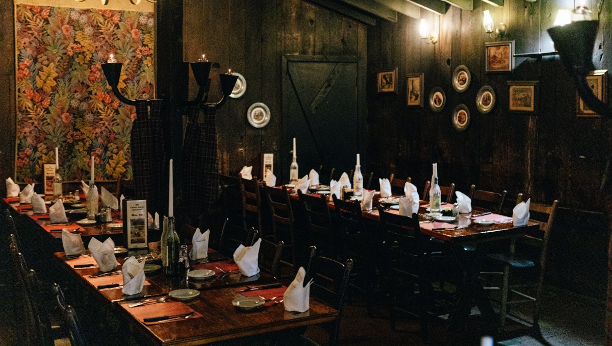 Interior of restaurant's dark dining with tables set and wall lamps lit