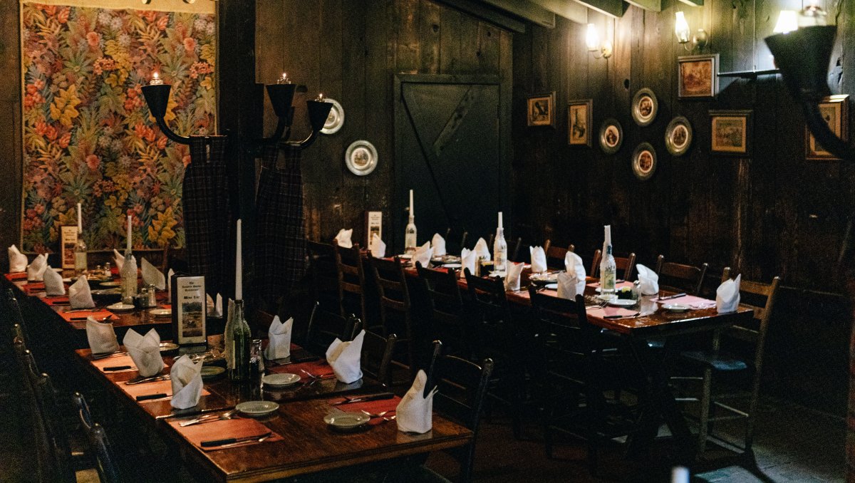 Interior of restaurant's dark dining with tables set and wall lamps lit