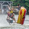 4 teens in lifejackets and bathing suites suspended mid-air as they tip out of their yellow and red tube on Badin Lake