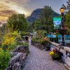 Couple admiring gardens on bridge, surrounded by plants and flowers with mountains in background as sun begins to set