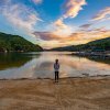 Child standing at edge of lake's beach with calm water, dock and shoreline in distance