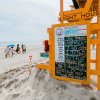 Orange lifeguard stand with family walking on sand and ocean to the left