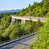 Linn Cove Viaduct surrounded by green trees and mountains in background on clear, bright day