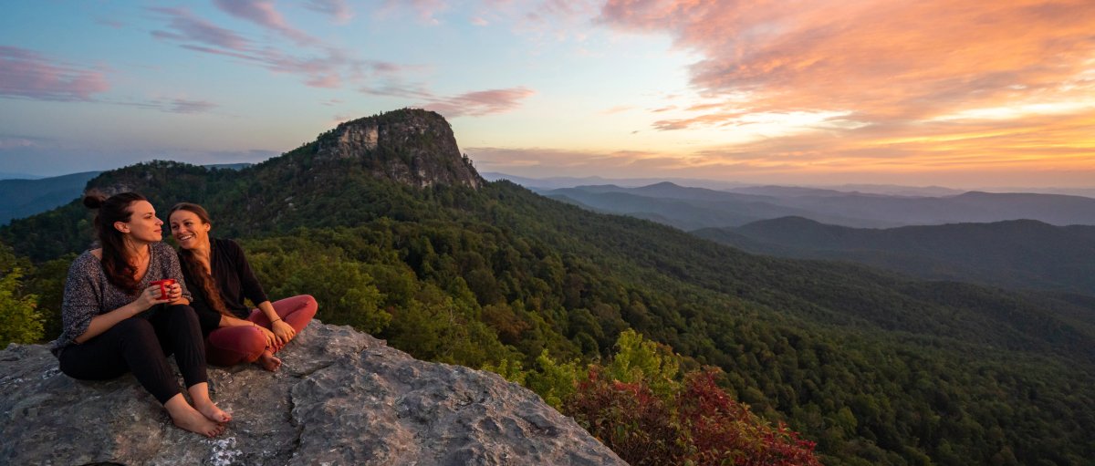 Two friends sitting on mountain taking in long-range views and sunrise