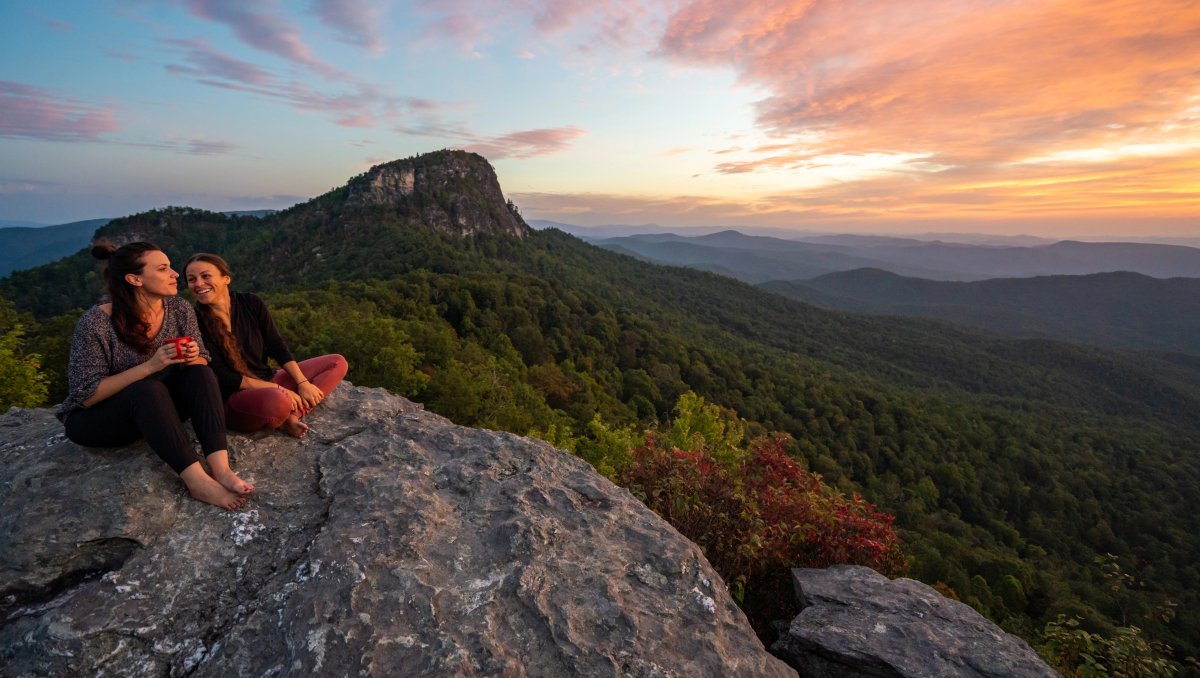 Two friends sitting on mountain taking in long-range views and sunrise