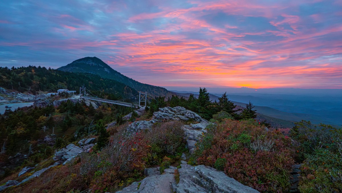 Aerial of Grandfather Mountain's Mile High Swinging Bridge during fall with bright sunset in distance