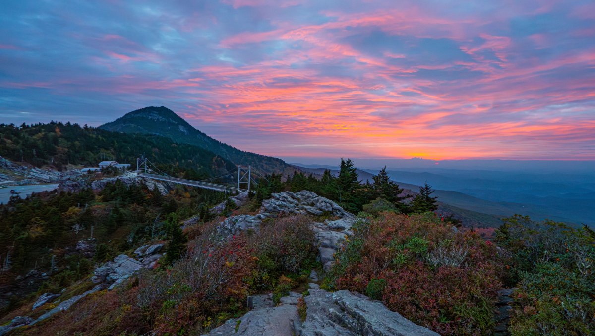 Aerial of Grandfather Mountain's Mile High Swinging Bridge during fall with bright sunset in distance