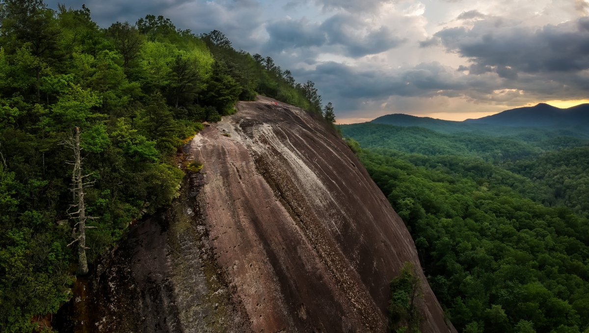 Huge mountain rock with green trees on it surrounded by other green mountains