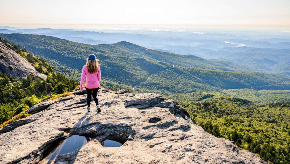 Woman walking atop Macrae Peak Lookout during summer on beautiful, clear day with mountains in background