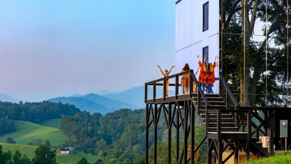 Friends on porch of mirror hotel with rolling hills and mountains in background