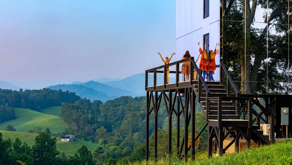 Friends on porch of mirror hotel with rolling hills and mountains in background