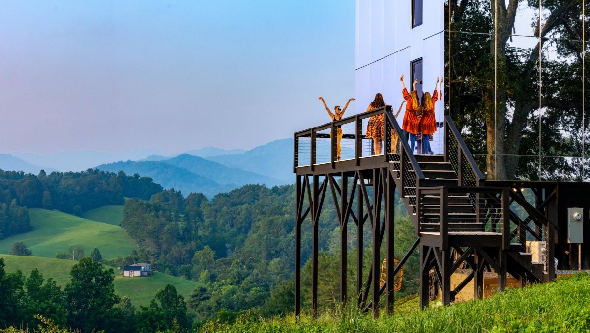 Friends on porch of mirror hotel with rolling hills and mountains in background