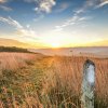 Sun rising over the mountains onto empty trail with brown grass on either side