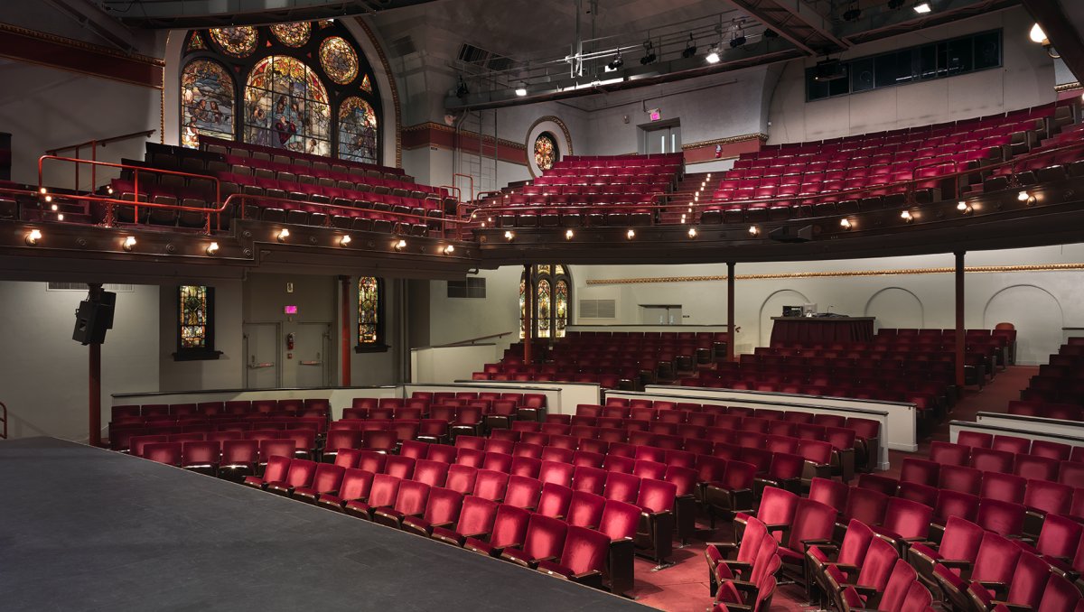 Empty theater with red seats and a balcony with stained glasses window against far wall