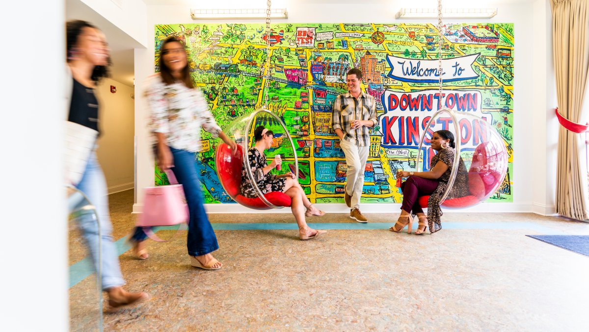 Friends sitting in hanging chairs in retro motel with colorful mural on wall in background