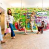 Friends sitting in hanging chairs in retro motel with colorful mural on wall in background