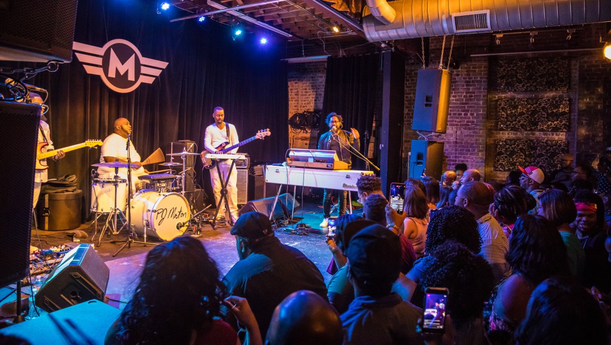 Band performing on stage inside building with lots of people in crowd