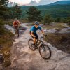 Two people mountain biking up mountain with mountains and trees in background