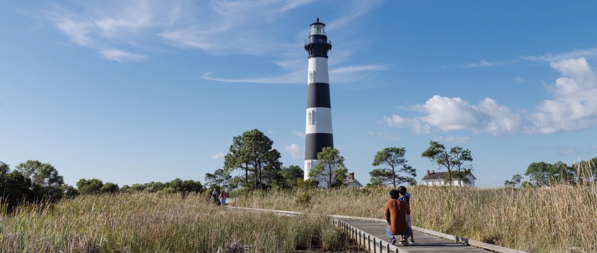 Father and son on walking back surrounded by marsh, admiring black and white lighthouse