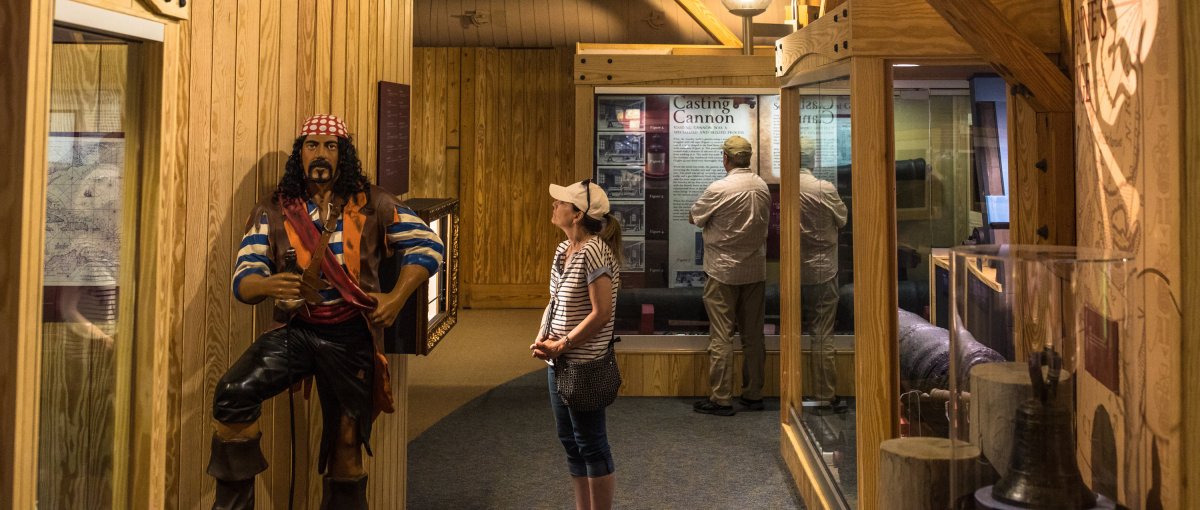 Woman looking at Blackbeard pirate replica inside maritime museum exhibit