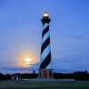 Cape Hatteras Lighthouse lit up at night with eerie moon in sky in background