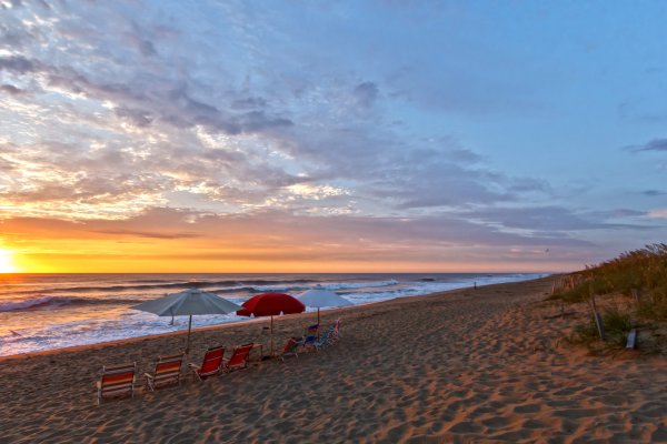 Beach chairs and umbrellas sitting in a row on an empty beach as the sun rises over the ocean