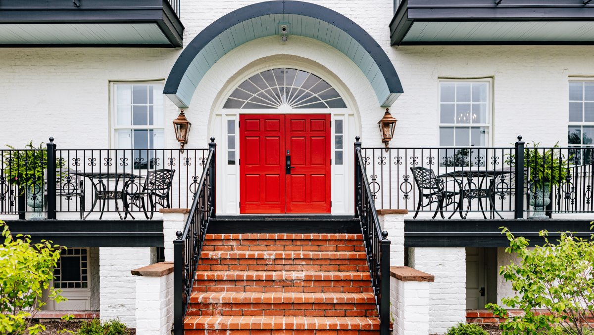 Exterior of white mansion inn with bright red door and brick steps leading to landing