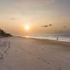 Sun rising in distance over wide-open beach with a few people walking on sand and rentals to left