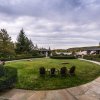 Four Adirondack chairs sitting on a green lawn looking out onto trees, lake and hills