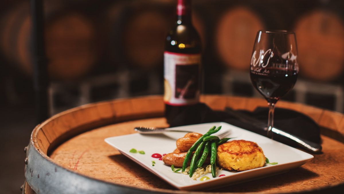 Small plate, glass of wine and wine bottle from Old North State Winery sitting on a wine barrel