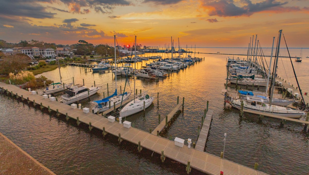 Many boats docked in a harbor with sun setting over water