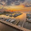 Many boats docked in a harbor with sun setting over water