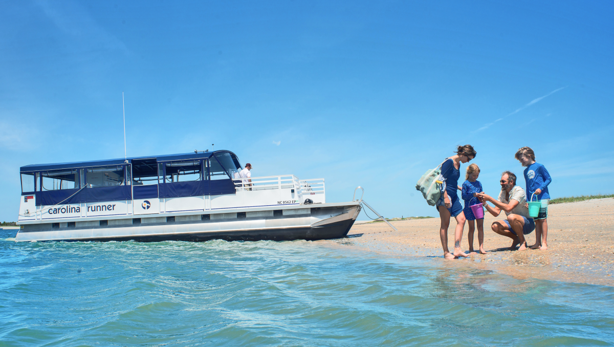 Family of four looking at shells on beach with boat in background