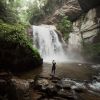 Woman walking on rocks with back to camera with beautiful waterfalls and rock walls and trees in background