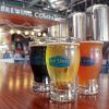 Closeup of three types of beers from Pitt Street Brewing with logos on mugs and patrons and brewery in background