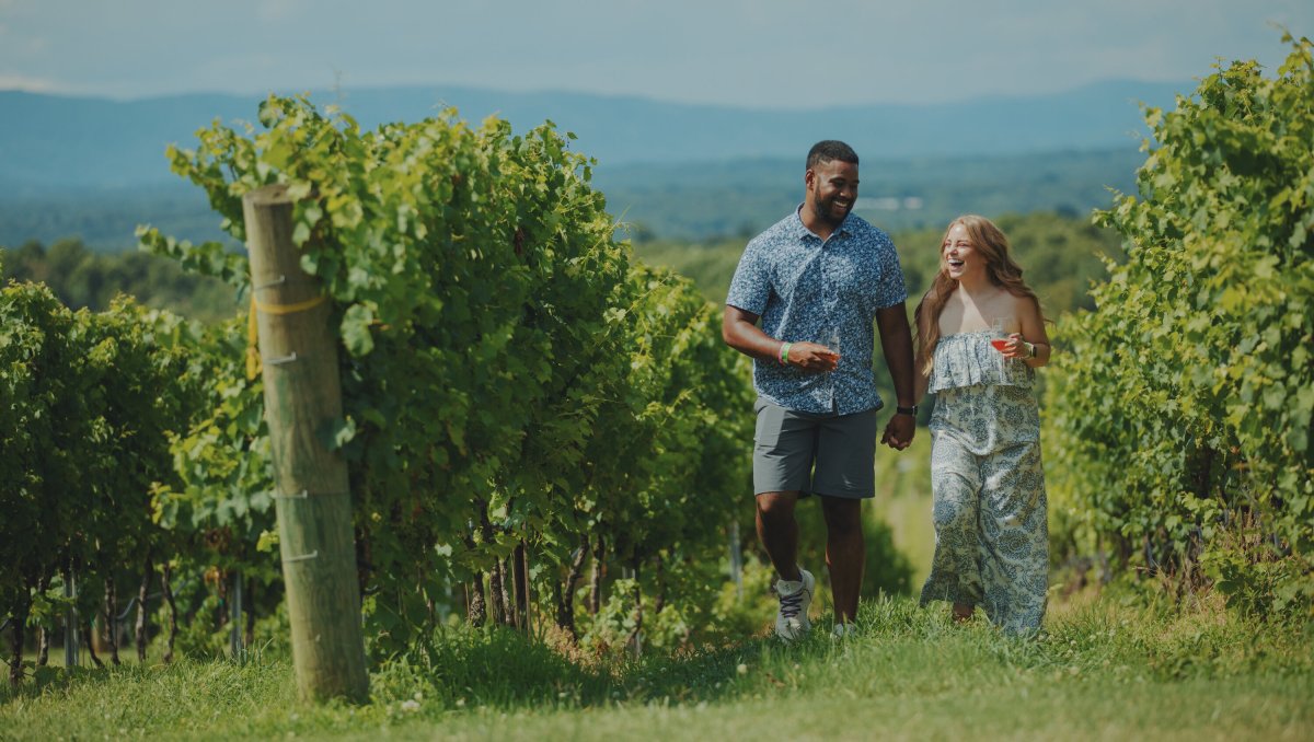 Smiling couple walking hand in hand through Raffaldini Vineyards' vineyard on sunny day