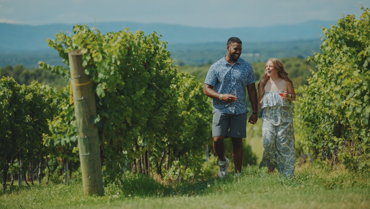 Smiling couple walking hand in hand through Raffaldini Vineyards' vineyard on sunny day