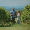 Couple holding hands and wine, laughing while walking through vineyard