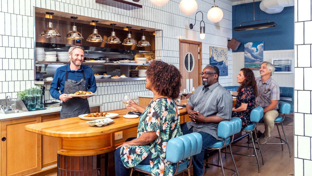 Diners sitting at bar of restaurant, talking with smiling bartender