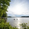 Two kayakers in distance paddling in open, calm lake with green trees framing foreground