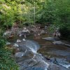 Sliding Rock with many people at bottom in natural pool, surrounded by green trees during daytime