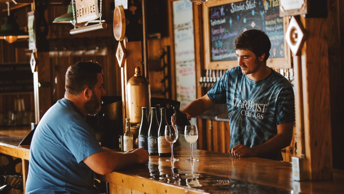 Man at Stardust Cellars bar sampling wine inside, wine maker pouring wine