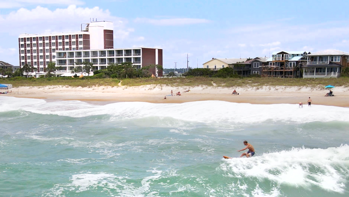 Man surfing in ocean in front of beach and resort