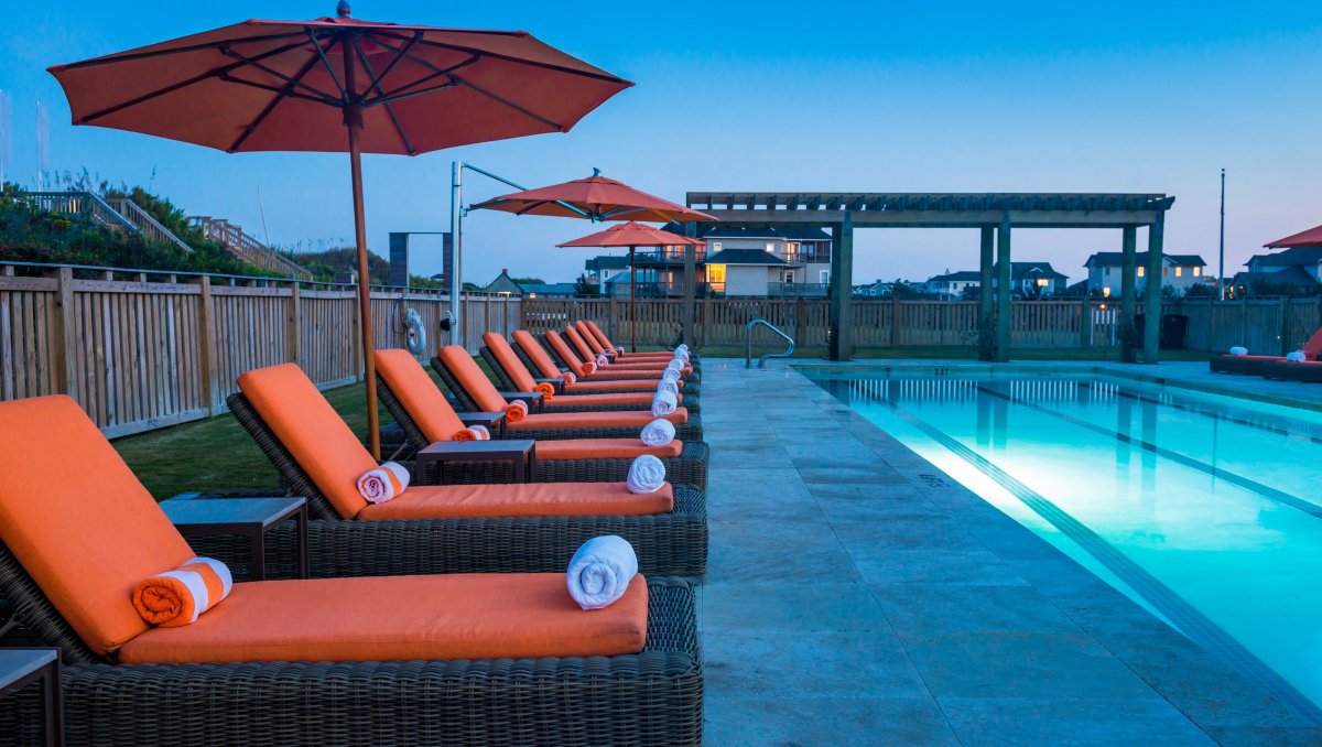 Long row of orange lounge chairs sitting by pool at dusk