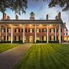 Exterior of grand, brick inn lit up at dusk with green grounds in foreground