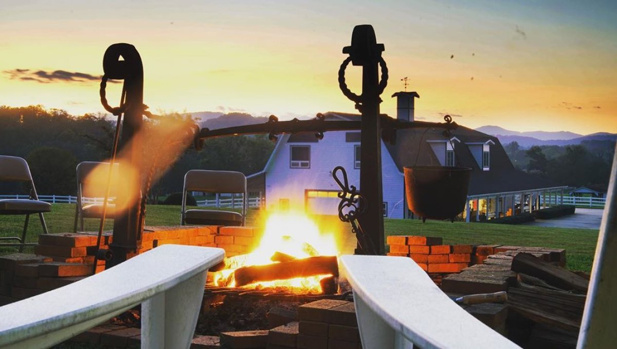 Chairs sitting around large patio fire with big barn and sunset in distance