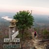 Person walking down trail with sign in foreground pointing to various mountains